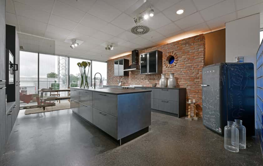 Große moderne und dunkle Küche vor Steinwand mit Kücheninsel und zwei Küchenzeilen sowie einem freistehenden Kühlschrank